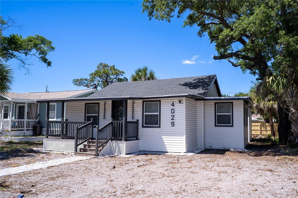 A white, single-story house with a dark-trimmed porch and roof stands on a sandy lot — 4029 13TH AVENUE S, ST PETERSBURG, FL