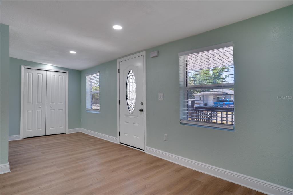 A room with light green walls, wood-look flooring, a white front door, and two windows — 4029 13TH AVENUE S, ST PETERSBURG, FL