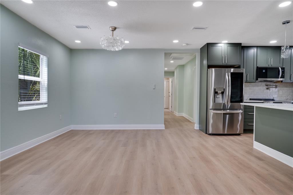 A dining area with light blue walls, wood-look flooring, and an adjacent kitchen with dark cabinets — 4029 13TH AVENUE S, ST PETERSBURG, FL