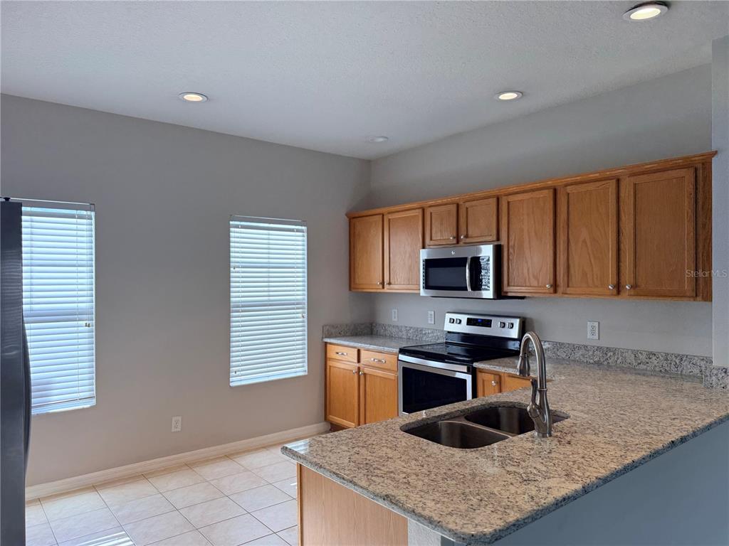 A kitchen features wood cabinets, granite countertops, stainless steel appliances, and tile flooring — 1110 OAK POND DRIVE, CELEBRATION, FL