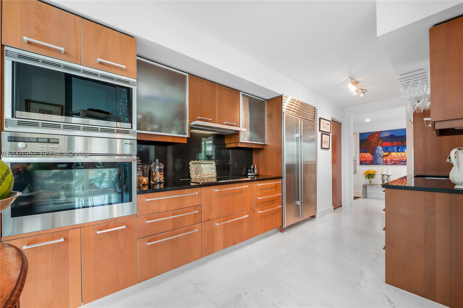 A modern kitchen features wood cabinets, stainless steel appliances, and black countertops on white flooring — 1331 Brickell Bay Dr # 408, Miami FL 33131, MIAMI, FL
