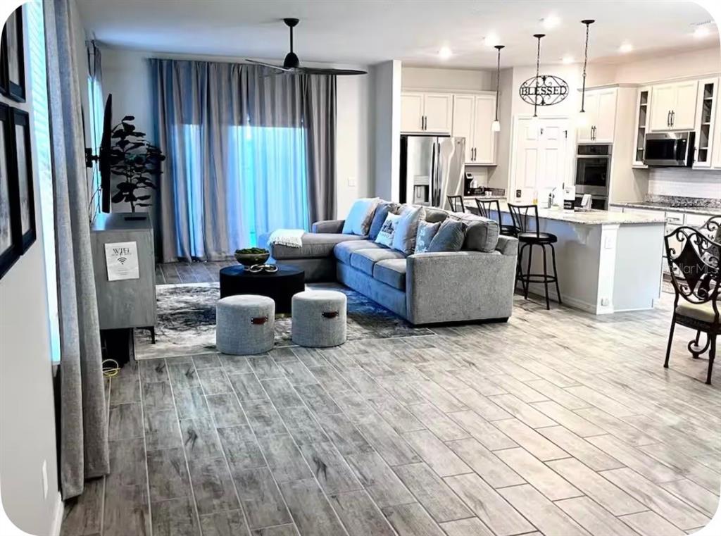 An open-concept living area features wood-look tile flooring, a gray sectional sofa, and a kitchen — 158 ABERDEEN STREET, DAVENPORT, FL