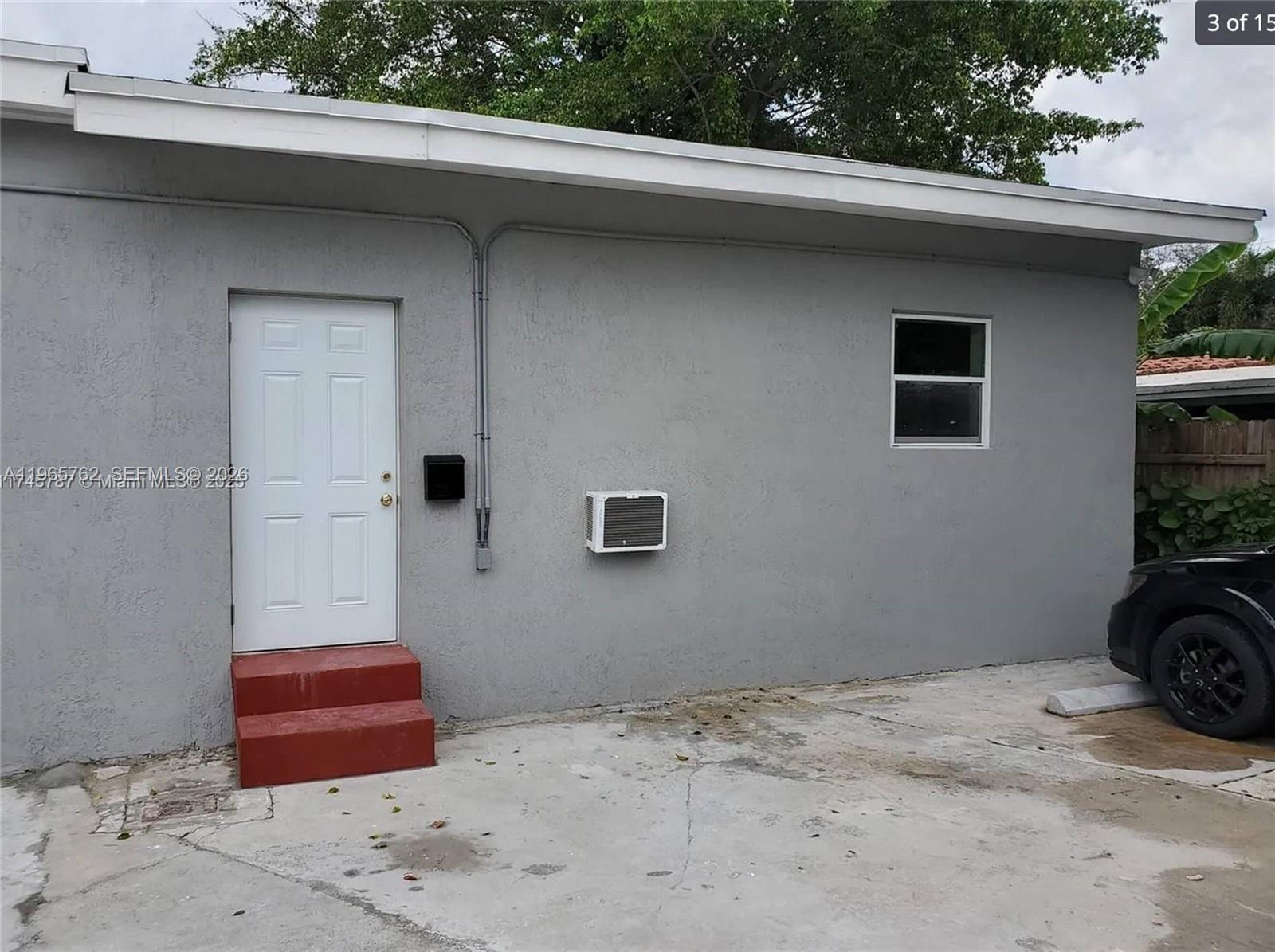 A grey exterior wall features a white door with red steps and a window — 2425 NW 28th St, Miami FL 33142, MIAMI, FL