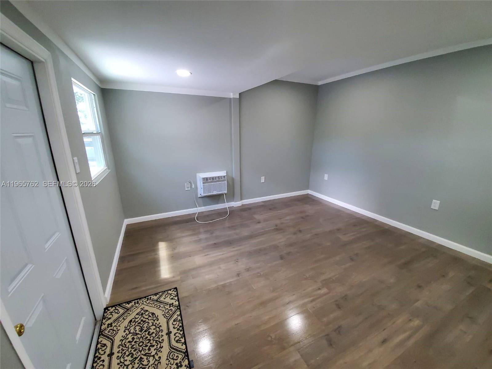 An empty room features gray walls, wood-look flooring, a window, and a wall-mounted air conditioner — 2425 NW 28th St, Miami FL 33142, MIAMI, FL