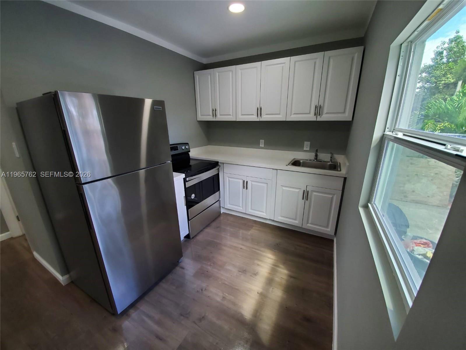 A small kitchen features white cabinets, stainless steel appliances, and wood-look flooring — 2425 NW 28th St, Miami FL 33142, MIAMI, FL