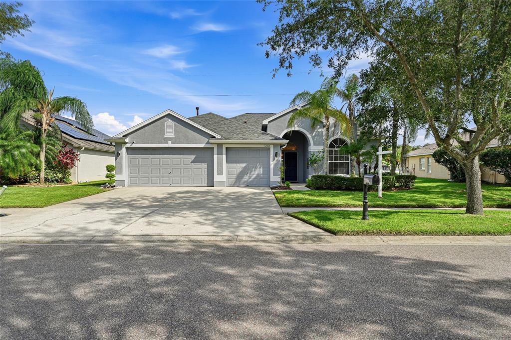A gray single-story house with a three-car garage and a paved driveway under a blue sky — 12018 NORTHUMBERLAND DRIVE, TAMPA, FL