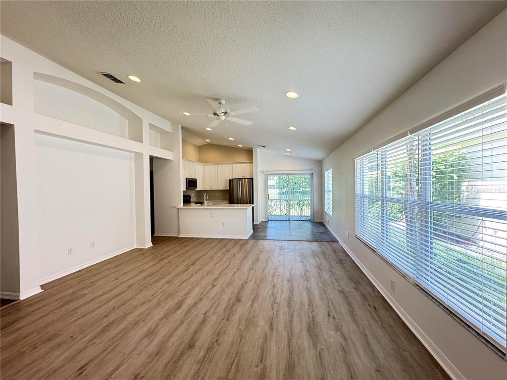 An open-concept living room with wood-look flooring, recessed lighting, and a kitchen in the background — 23741 CORAL RIDGE LANE, LAND O LAKES, FL