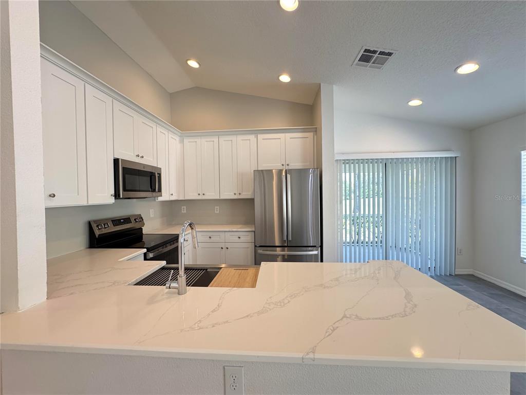 A kitchen features white cabinets, stainless steel appliances, and a large quartz-topped island — 23741 CORAL RIDGE LANE, LAND O LAKES, FL