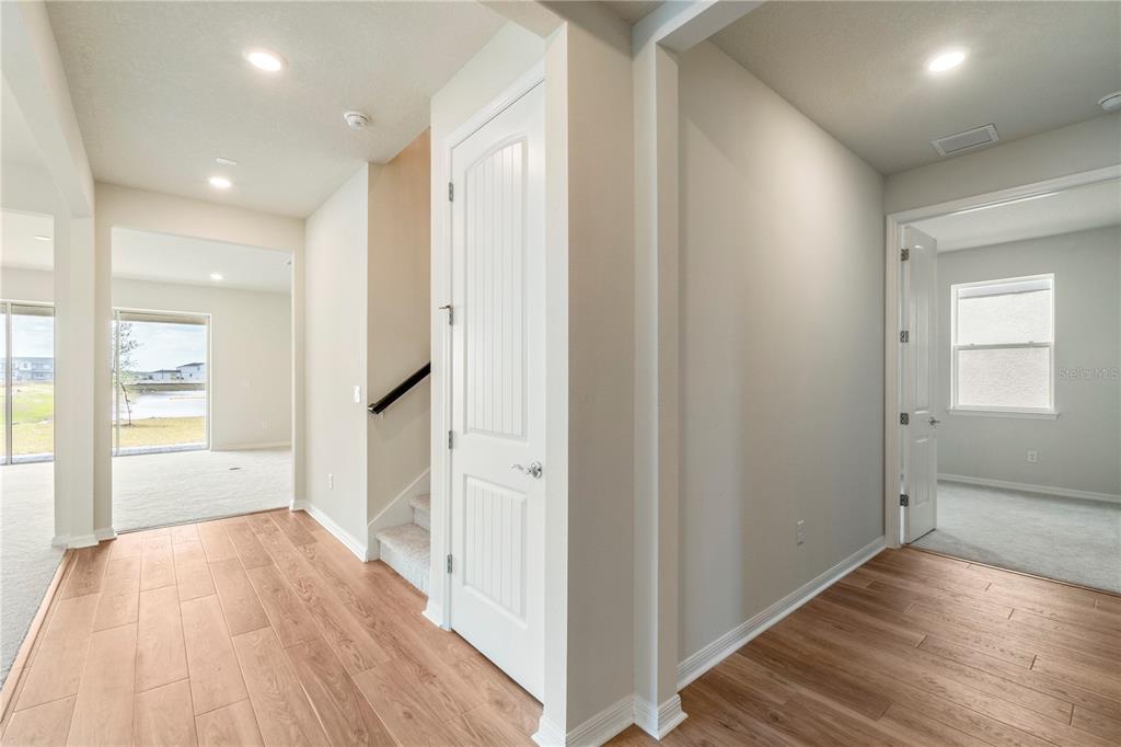 A hallway with wood-look flooring leads to a staircase, a closed door, and two rooms — 9662 PASSAIC PARKWAY, ORLANDO, FL