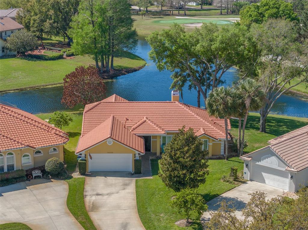 An aerial view of a yellow house with a tile roof, driveway, and backyard pond — 14050 FAIRWAY WILLOW LANE, WINTER GARDEN, FL