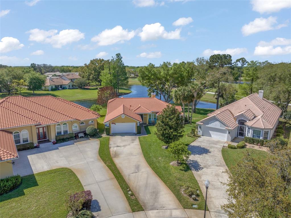 An aerial view shows three suburban houses with tile roofs and driveways near a pond — 14050 FAIRWAY WILLOW LANE, WINTER GARDEN, FL