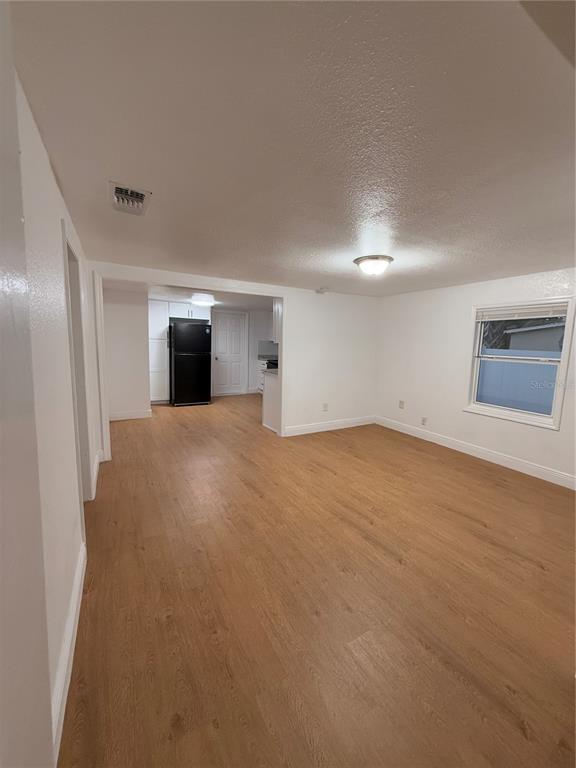An open-concept room with light wood-look flooring leads into a kitchen with a black refrigerator — 636 COKE AVENUE, WINTER GARDEN, FL