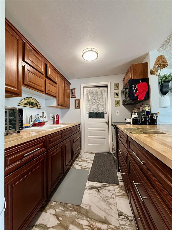 A galley kitchen features dark wood cabinets, light wood countertops, and white marble-patterned flooring — 4926 FILNER STREET, NEW PORT RICHEY, FL