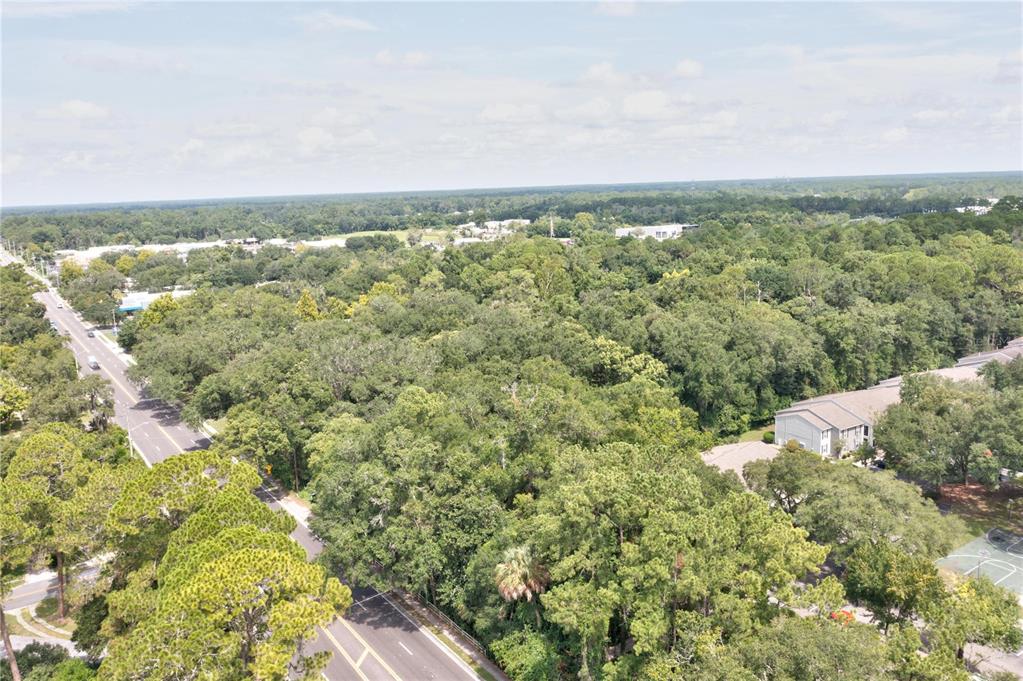 An aerial view shows a wooded lot bordered by a road and apartment buildings — 780 NE 23RD AVENUE, GAINESVILLE, FL