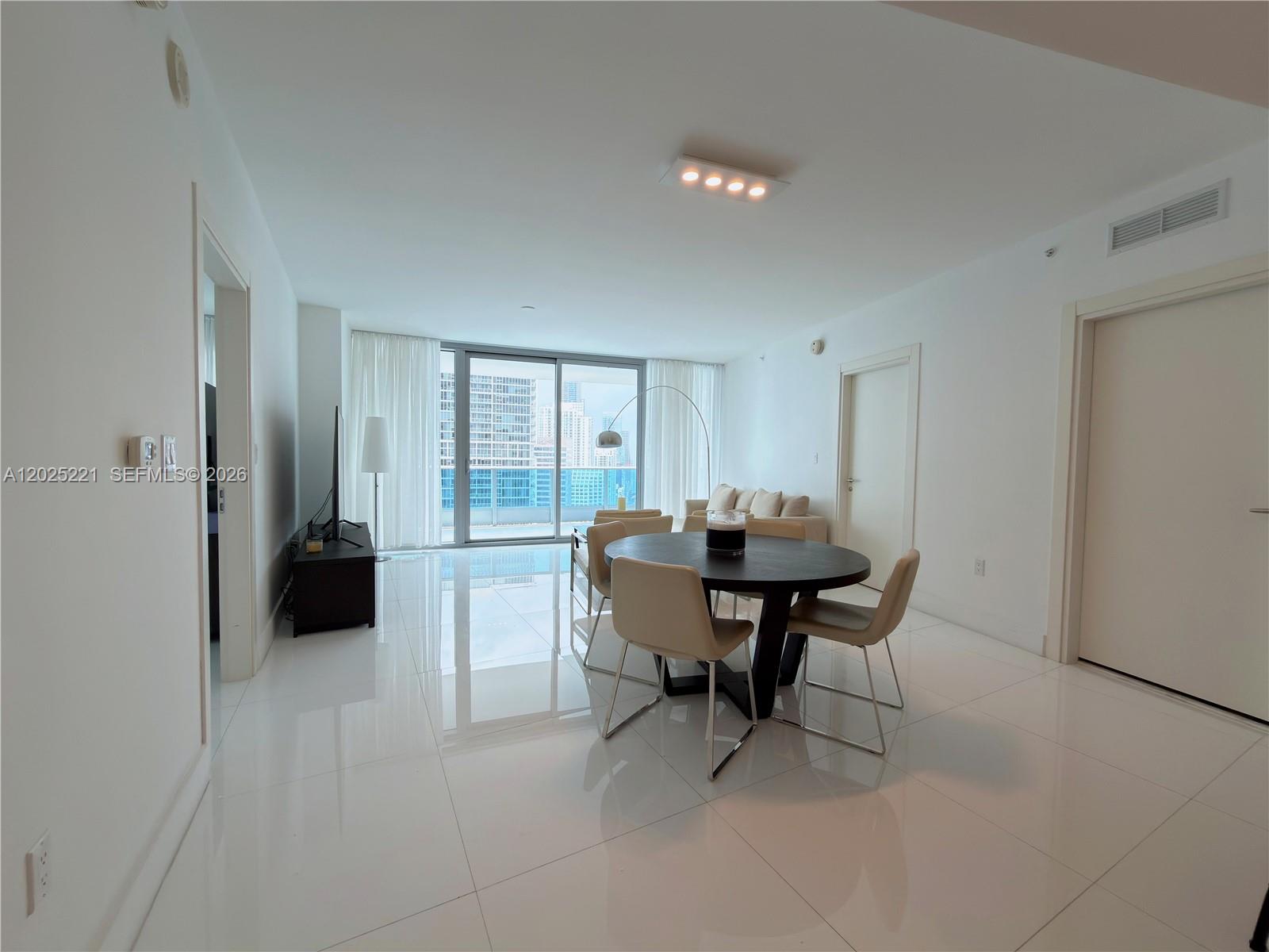 A bright living and dining area features white tile floors, modern furniture, and balcony access — 200 Biscayne Boulevard Way # 4104, Miami FL 33131, MIAMI, FL