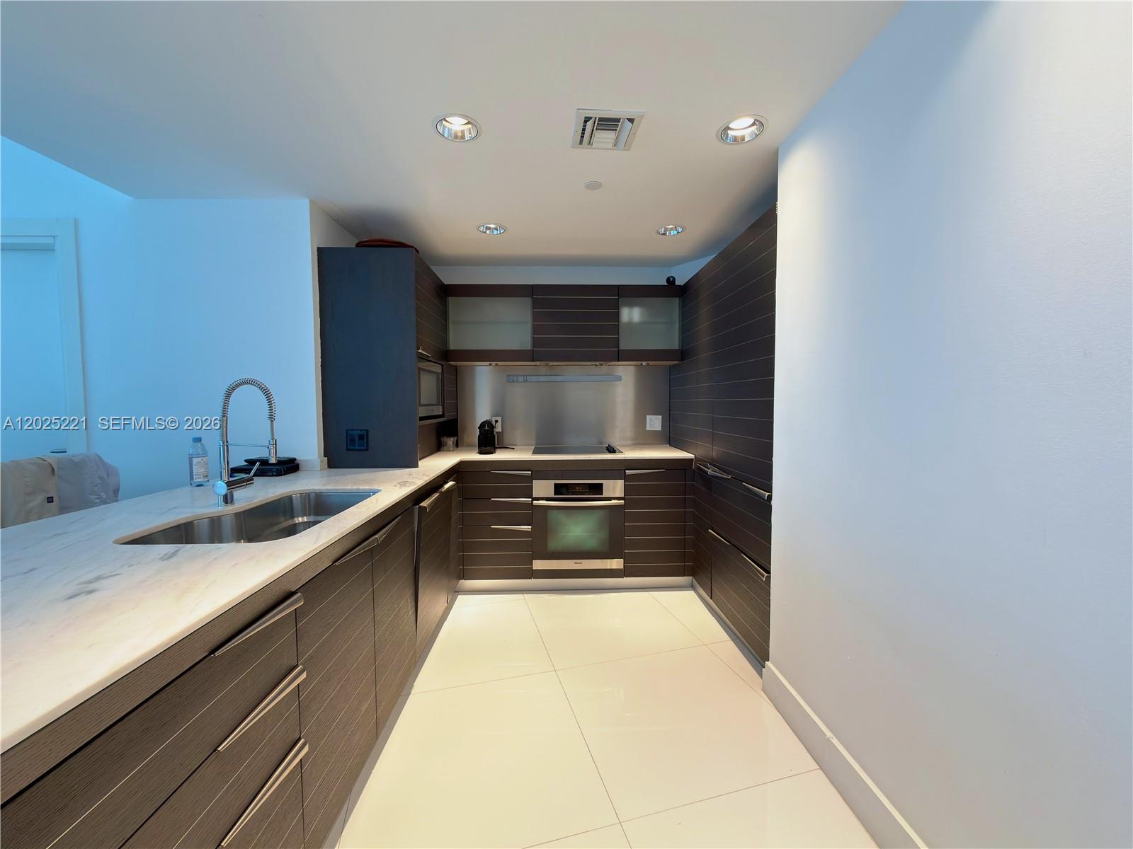 A modern galley kitchen features dark wood cabinetry, white marble countertops, and stainless steel appliances — 200 Biscayne Boulevard Way # 4104, Miami FL 33131, MIAMI, FL