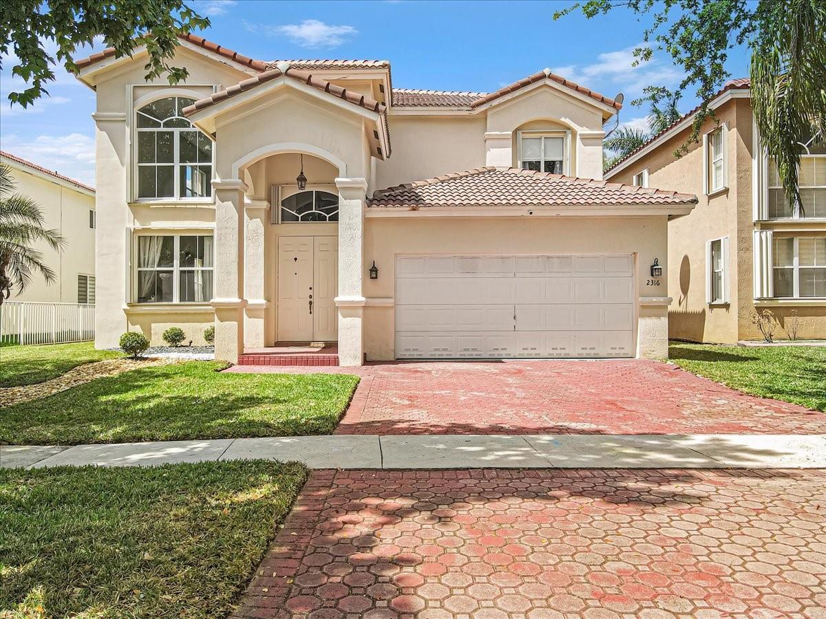 A two-story house with a beige stucco exterior, a tiled roof, and a paved driveway — 2316 SW 127th Avenue, Miramar FL 33027, MIRAMAR, FL