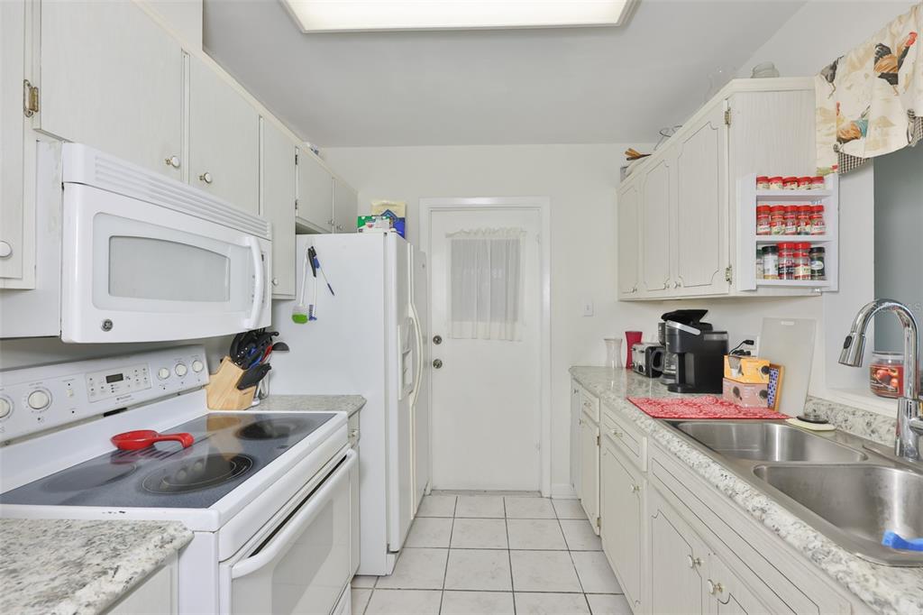 A galley kitchen features white cabinets, white appliances, speckled countertops, and a tiled floor — 700 RUTGERS PLACE, SUN CITY CENTER, FL