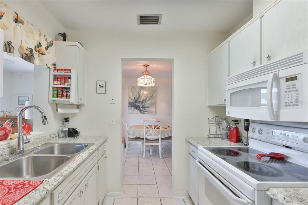A kitchen with white cabinets, granite countertops, and a view into a dining area — 700 RUTGERS PLACE, SUN CITY CENTER, FL
