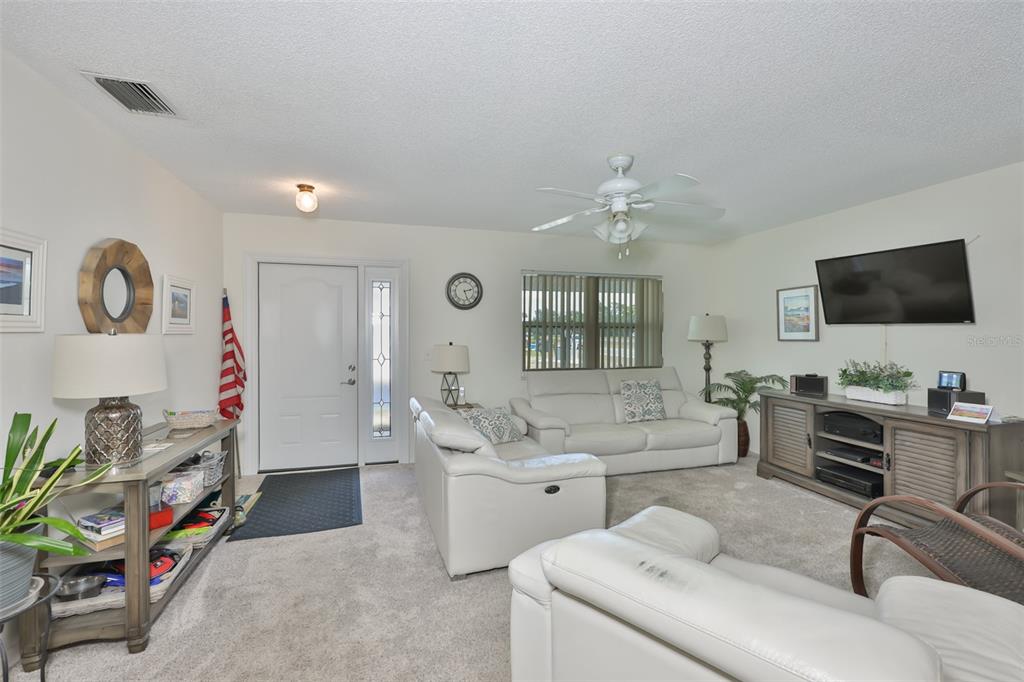 A living room features white leather sofas, a television console, and a front entryway door — 700 RUTGERS PLACE, SUN CITY CENTER, FL