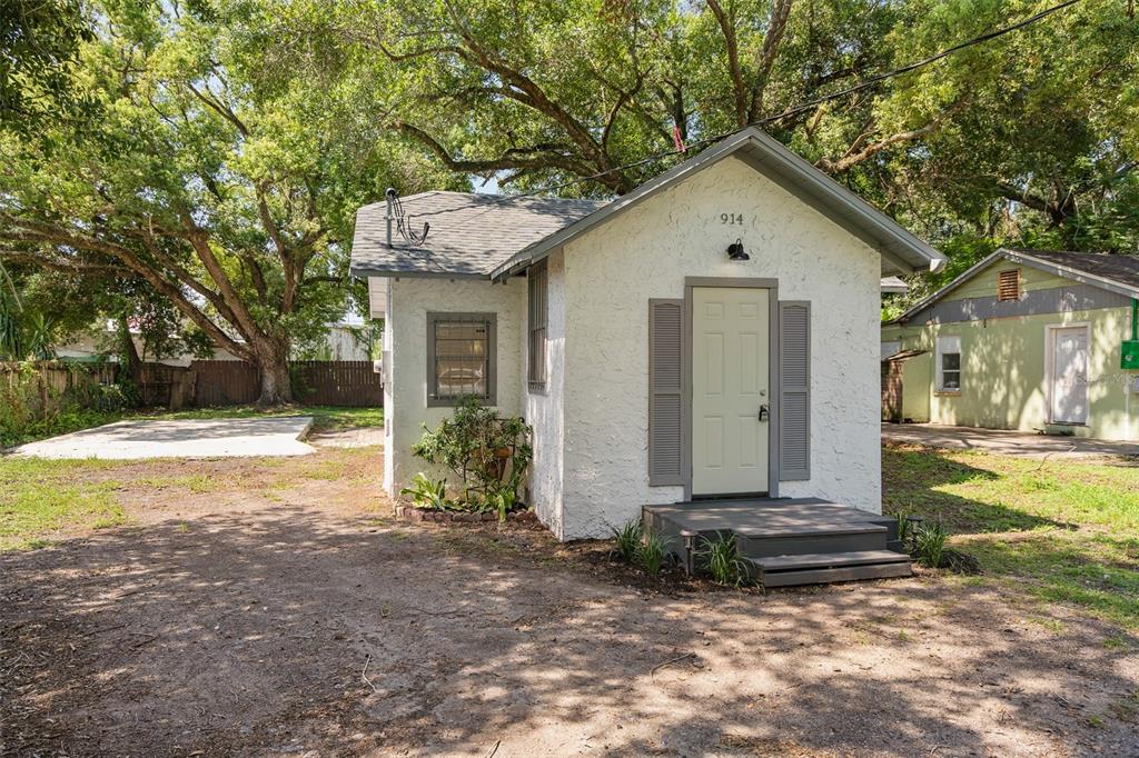 A small, white stucco cottage with a gray front door and steps stands on dirt — 914 26TH STREET, ORLANDO, FL