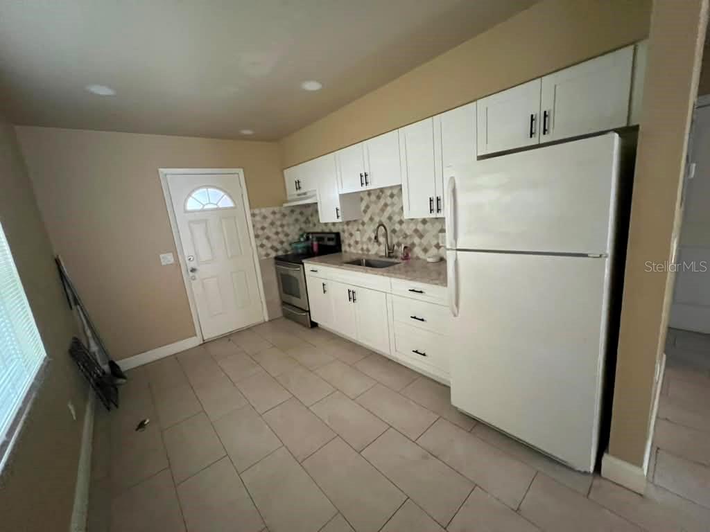 A kitchen features white cabinets, a white refrigerator, a stainless steel stove, and tiled flooring — 10106 N 10TH STREET UNIT A, TAMPA, FL