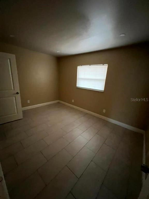 An empty bedroom features beige walls, light-colored tile flooring, and a single window with blinds — 10106 N 10TH STREET UNIT A, TAMPA, FL