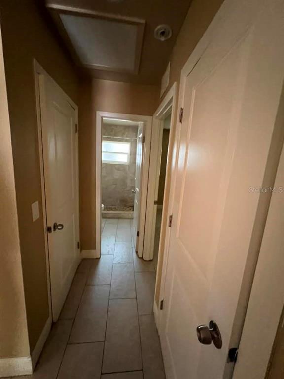 A hallway with light-colored tile flooring leads to a bathroom with a tiled shower — 10106 N 10TH STREET UNIT A, TAMPA, FL