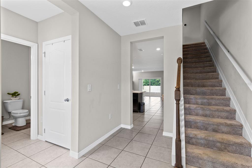 An entryway features a tiled floor, a half bathroom, a staircase, and a rear view — 4827 CORAL CASTLE DRIVE, KISSIMMEE, FL