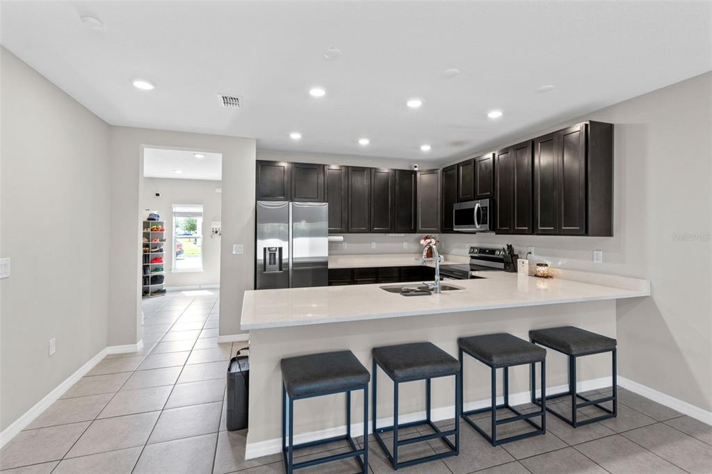 A kitchen features dark wood cabinets, light countertops, a breakfast bar with stools, and tile flooring — 4827 CORAL CASTLE DRIVE, KISSIMMEE, FL