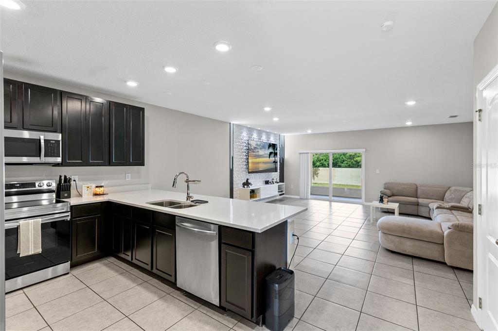 An open-concept kitchen with dark cabinets and white countertops flows into a tiled living area — 4827 CORAL CASTLE DRIVE, KISSIMMEE, FL