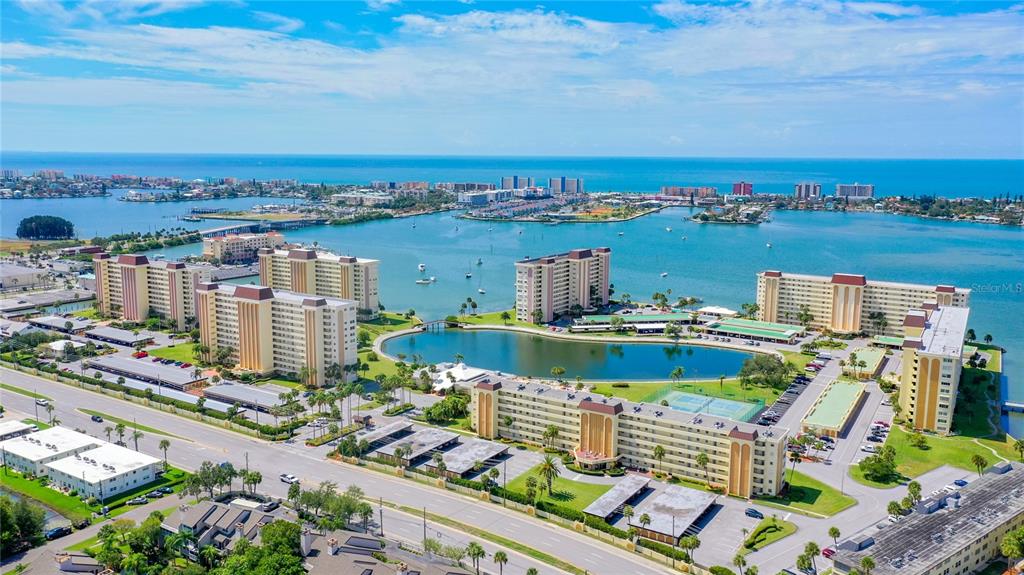 An aerial view shows multiple high-rise apartment buildings surrounding a central lake near the ocean — 4575 COVE CIRCLE UNIT 309, ST PETERSBURG, FL