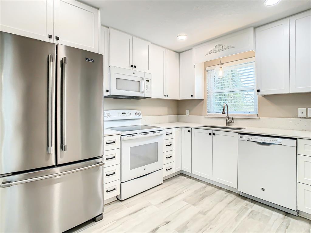 A modern kitchen features white cabinetry, stainless steel appliances, and light-colored wood-look tile flooring — 4575 COVE CIRCLE UNIT 309, ST PETERSBURG, FL