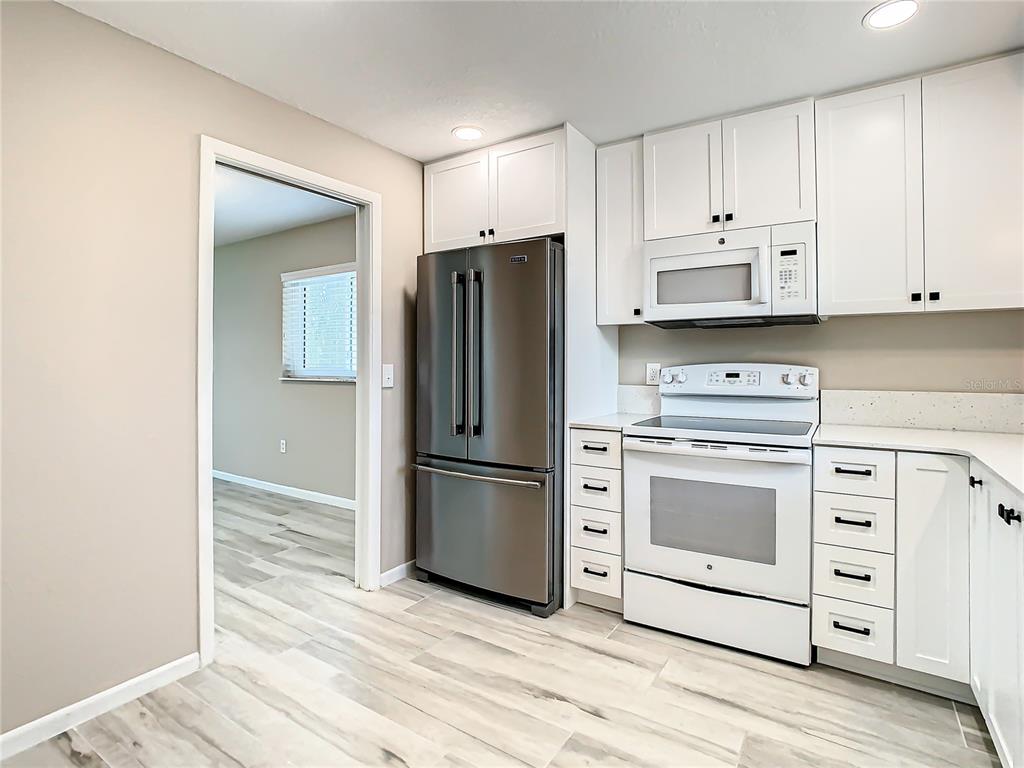 A kitchen with white cabinets, stainless steel refrigerator, white range, and light wood-look flooring — 4575 COVE CIRCLE UNIT 309, ST PETERSBURG, FL