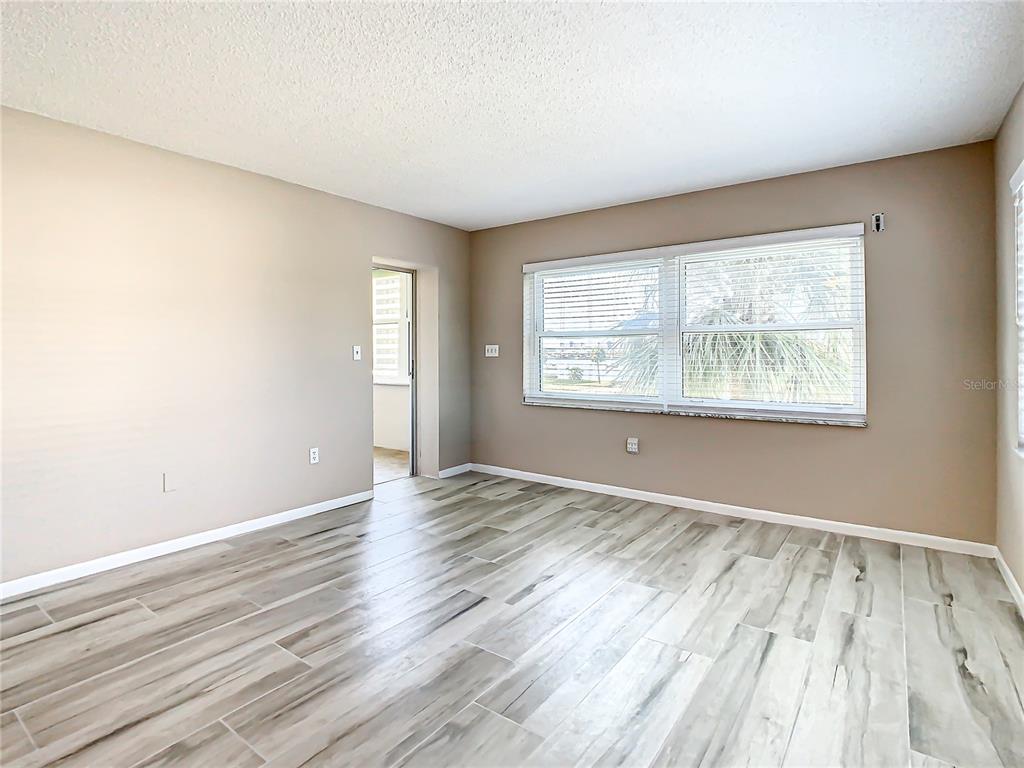An empty room features light-colored wood-look tile flooring, beige walls, and a large window — 4575 COVE CIRCLE UNIT 309, ST PETERSBURG, FL