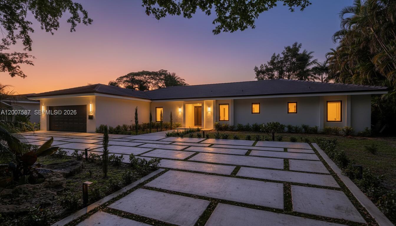 A modern single-story house at dusk features a large concrete paver driveway and landscaping — 1520 Lugo Ave, Coral Gables FL 33156, CORAL GABLES, FL