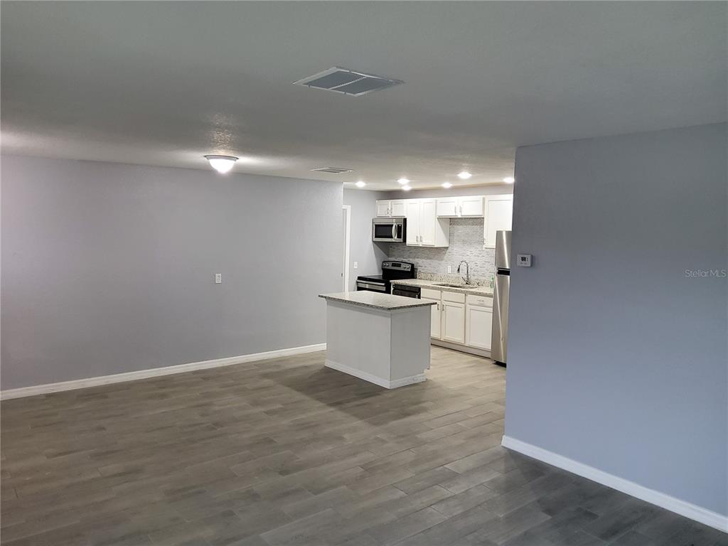 An open-concept kitchen with white cabinets and a small island overlooks a gray living area — 415 KING STREET, LAKE WALES, FL