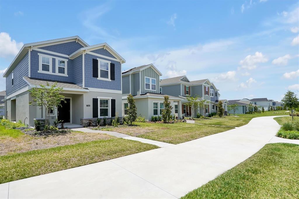 A row of suburban houses with blue and gray siding sits along a concrete sidewalk — 7245 SIENNA OAK ALLEY, ORLANDO, FL