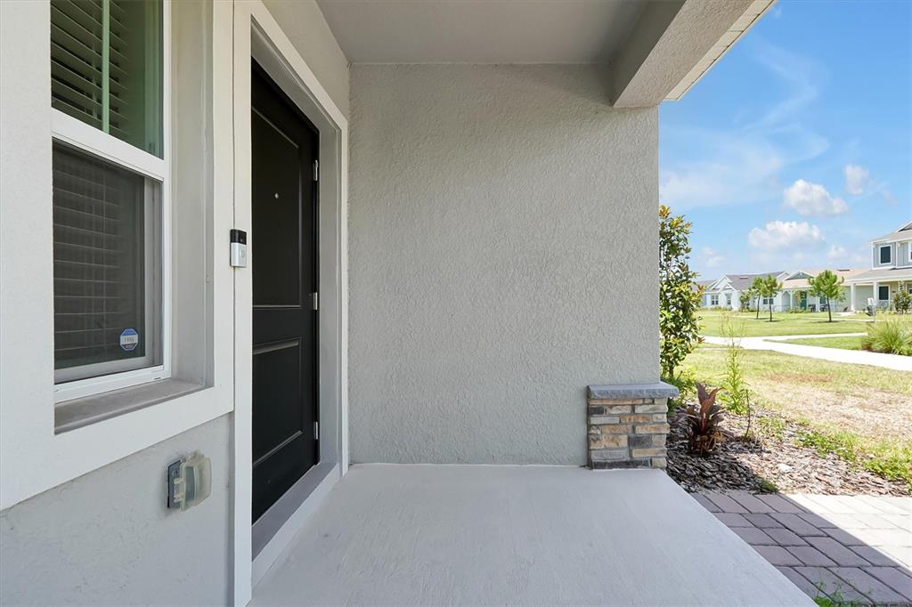 A covered front porch features a black door, a window, and a stone-accented pillar — 7245 SIENNA OAK ALLEY, ORLANDO, FL