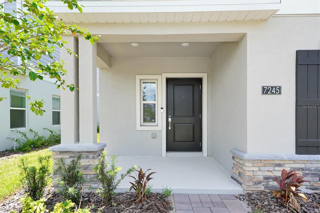The exterior of a house features a covered entryway with a black door and stone accents — 7245 SIENNA OAK ALLEY, ORLANDO, FL