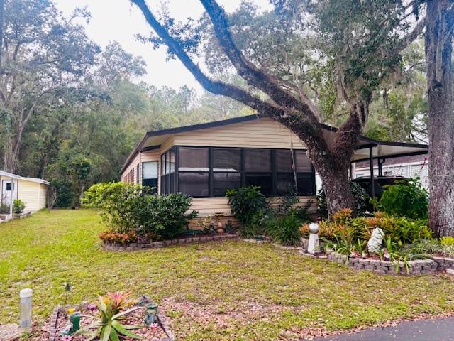 A single-story house with tan siding and a large tree in the front yard — 7053 SPANISH MOSS LANE, BROOKSVILLE, FL