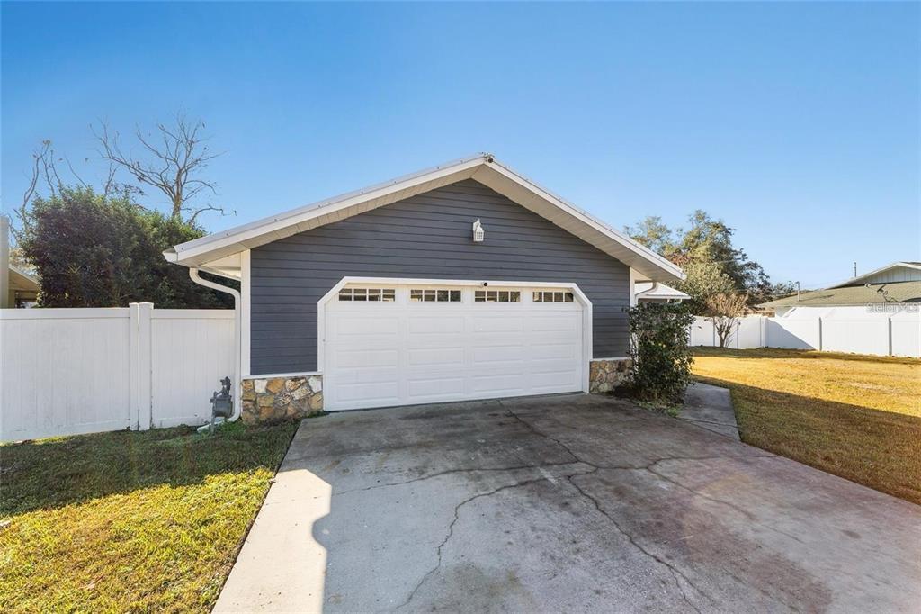A detached garage with dark gray siding, stone accents, and a white sectional door — 2700 SE 35TH STREET, OCALA, FL