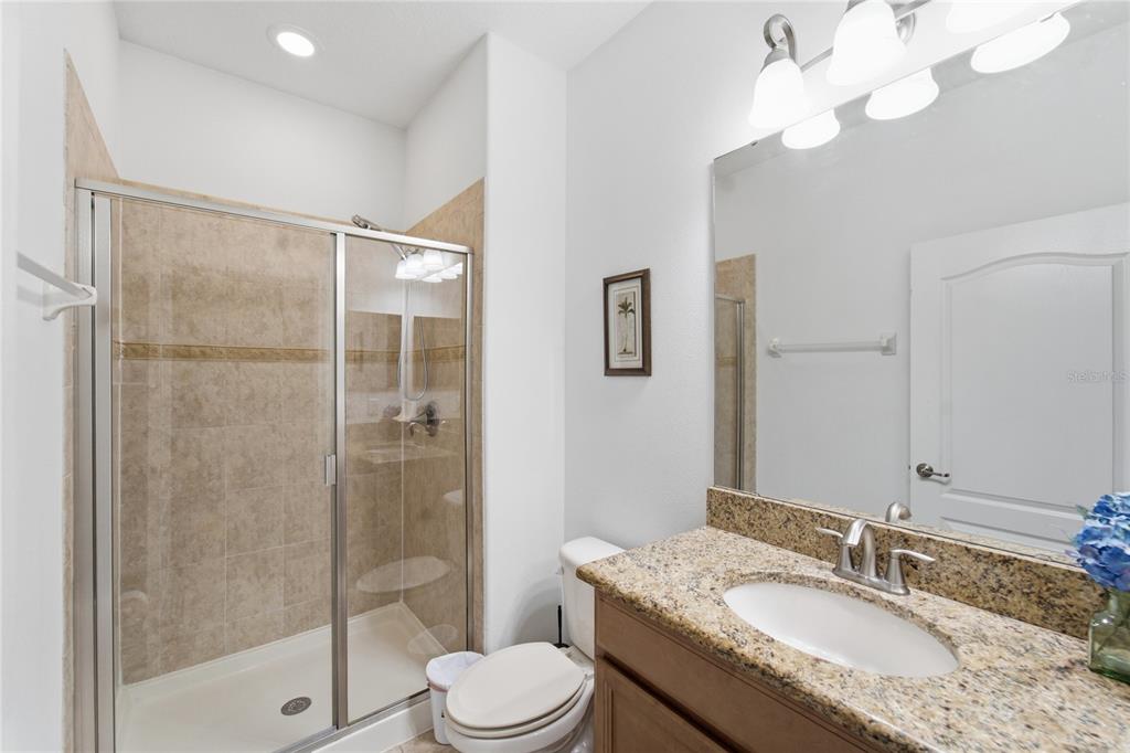 A bathroom features a glass-enclosed shower, a granite vanity countertop, and a white toilet — 3045 BEACH PALM AVENUE, KISSIMMEE, FL
