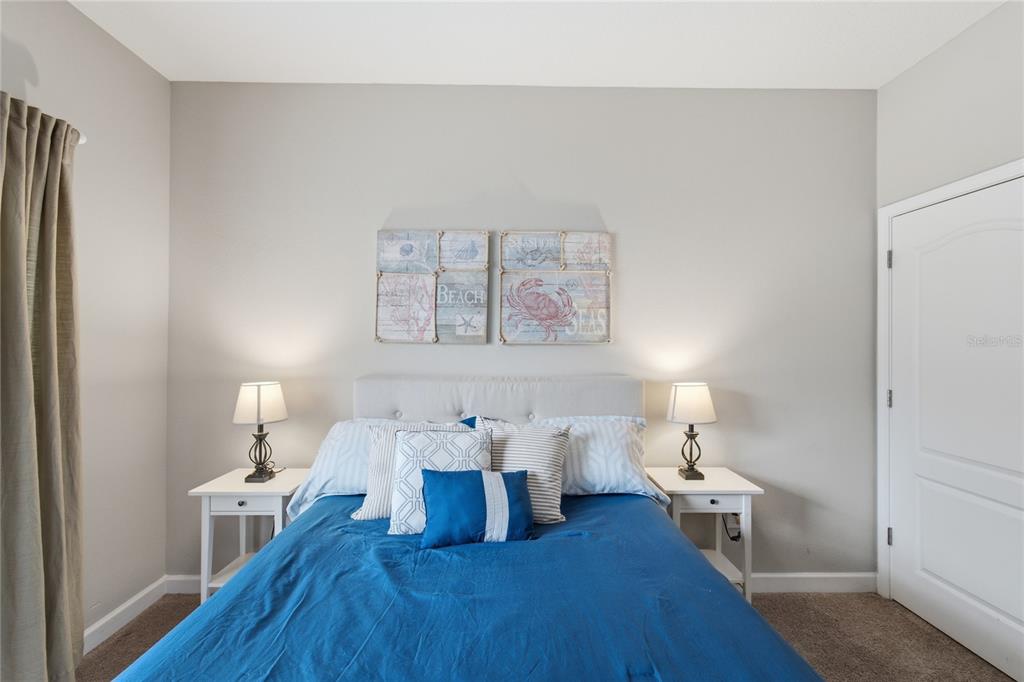 A bedroom features a bed with a blue comforter, two nightstands, and beach-themed wall art — 3045 BEACH PALM AVENUE, KISSIMMEE, FL