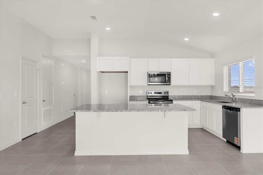 A kitchen features white cabinets, granite countertops, a center island, and gray tile flooring — 316 SUNBROOK DRIVE, GROVELAND, FL