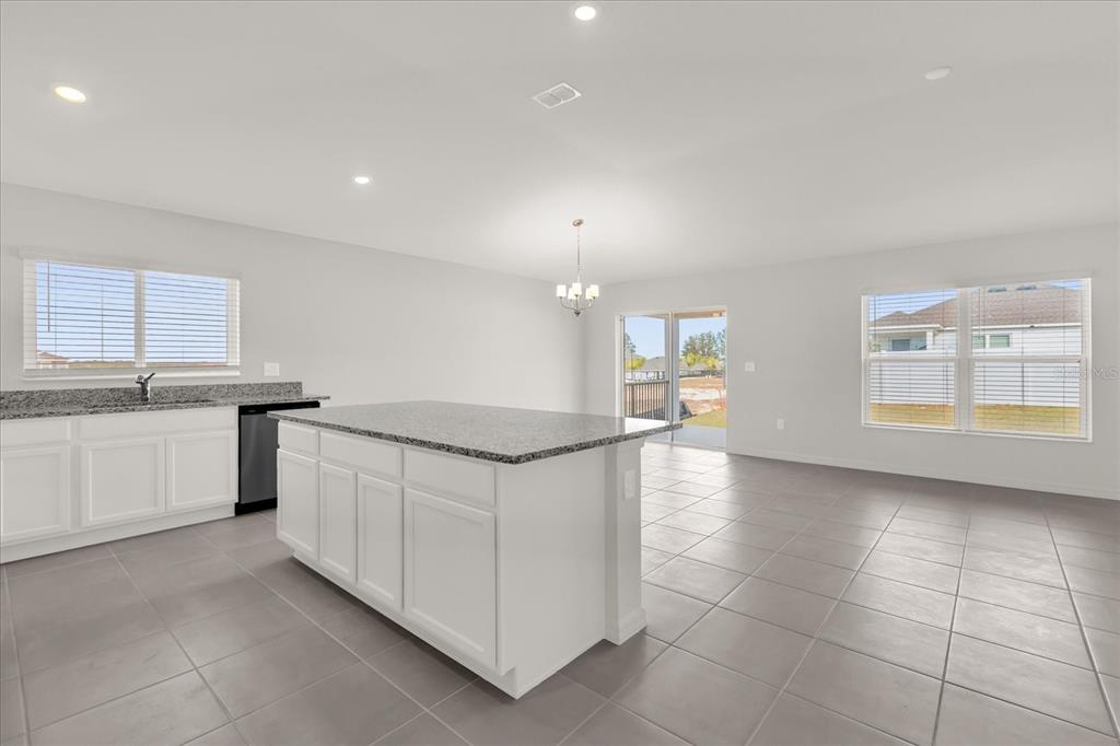A kitchen with a granite-topped island, white cabinets, and tile flooring opens to a dining area — 316 SUNBROOK DRIVE, GROVELAND, FL