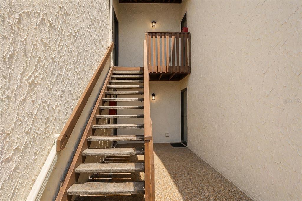 An outdoor staircase leads to an upper-level balcony between two stucco walls — 723 115TH AVENUE N UNIT 2106, ST PETERSBURG, FL
