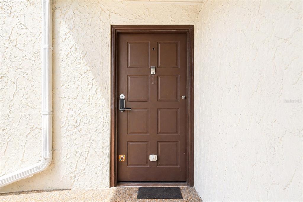 A brown six-panel front door is set into a textured beige stucco exterior wall — 723 115TH AVENUE N UNIT 2106, ST PETERSBURG, FL