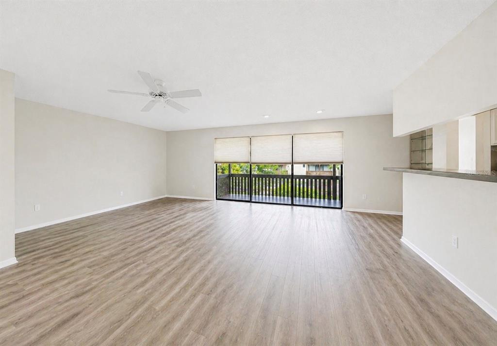An empty living room features light wood-look flooring, a ceiling fan, and a sliding glass door — 723 115TH AVENUE N UNIT 2106, ST PETERSBURG, FL