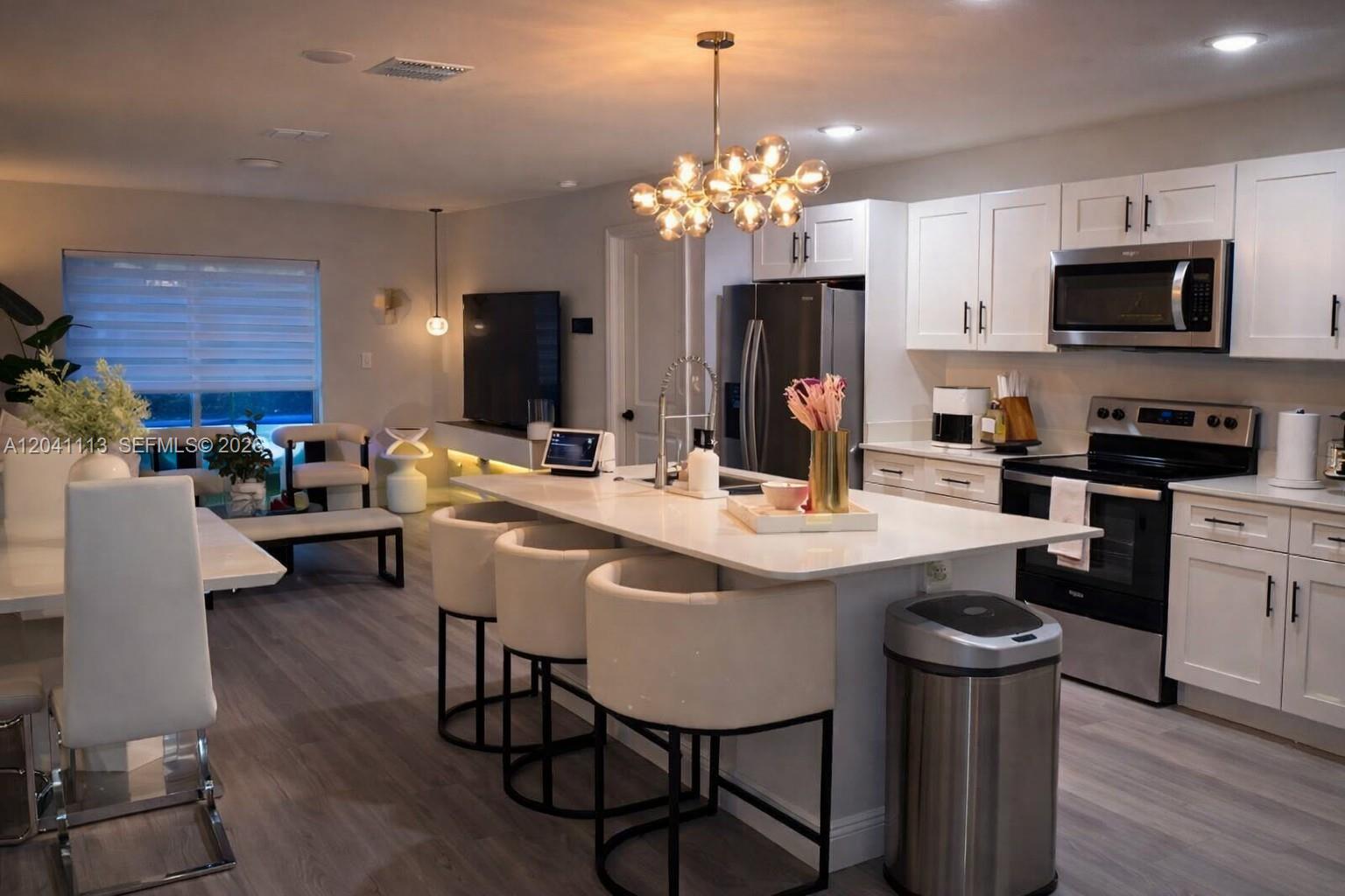 A modern kitchen features white cabinetry, a central island with bar stools, and stainless appliances — 39 REDWOOD TRACK RUN, Ocala FL 34472, OCALA, FL